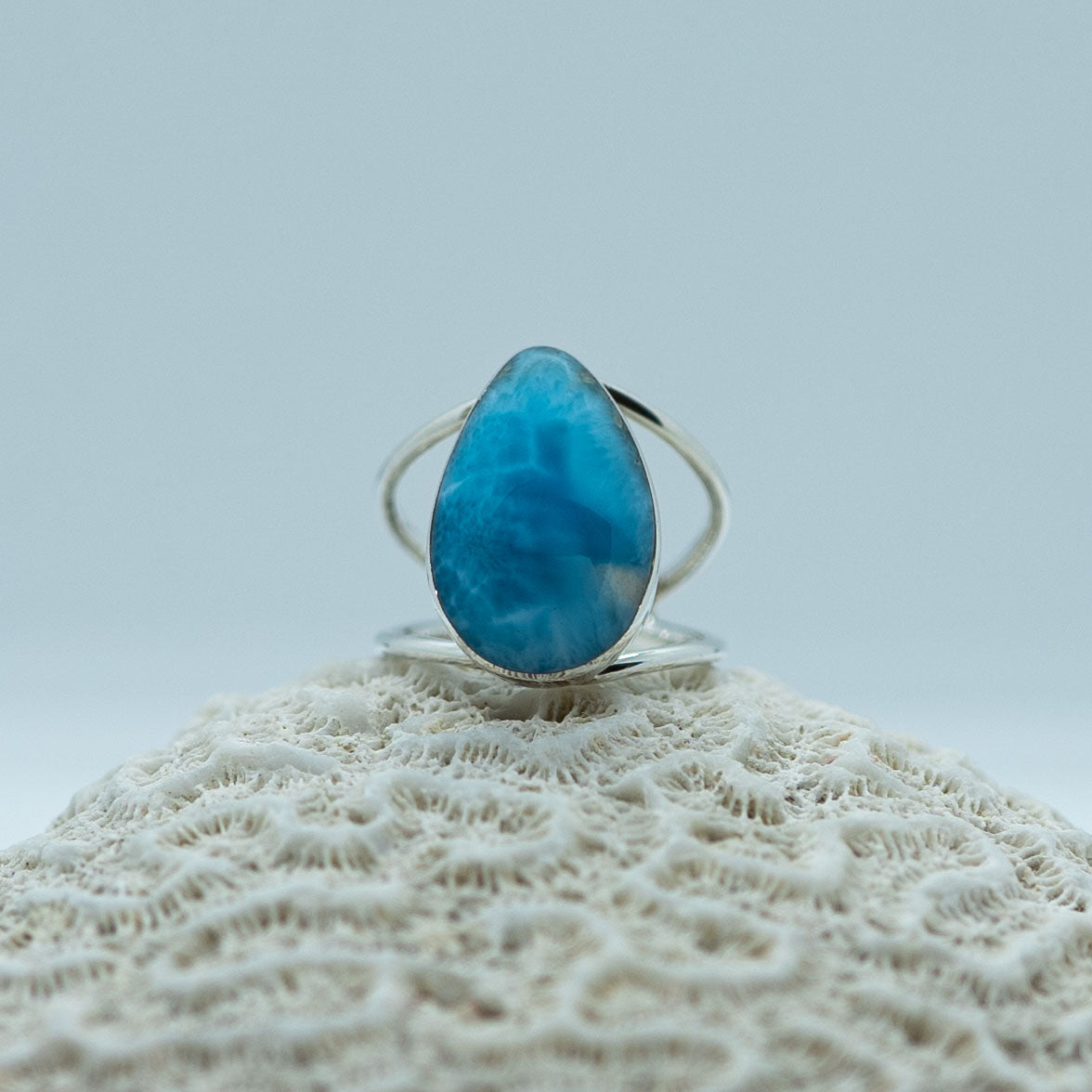Photo d'une bague en argent posée sur un coquillage. Cette bague est ornée d'une magnifique pierre de larimar en forme de goutte, elle est réglable pour s'adapter à plusieurs tailles de doigts