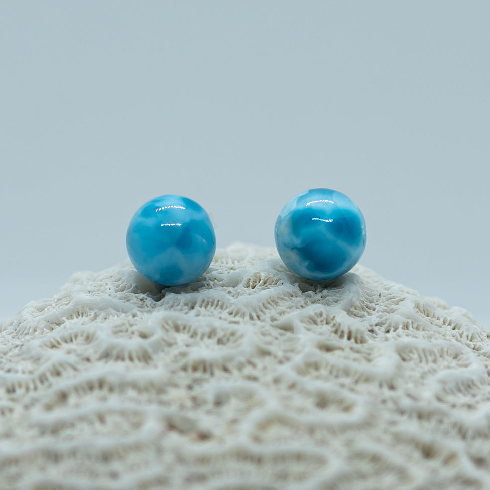 Photo de deux perles vue de face, posées sur un coquillage. La perle de gauche est d'un bleu ciel uniforme tandis que la perle de droite possède plusieurs nuance de bleu allant jusqu'au bleu foncé.