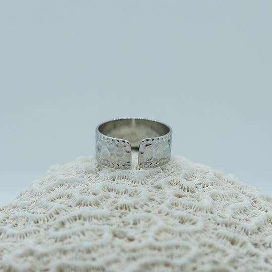 Bague ouverte et réglable en acier inoxydable 316L. Bague texturé avec un look tendance de couleur argenté, une breloque Orparima et une perle de larimar sont accrochés à la bague.