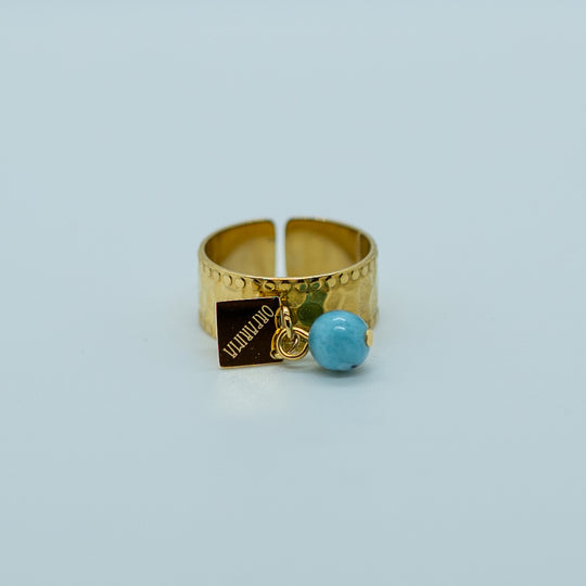 Bague en acier inoxydable 316L de couleur dorée avec une perles de larimar et une breloque Orparima accrochés au corps de la bague. Bague texturée au design tendance réglable