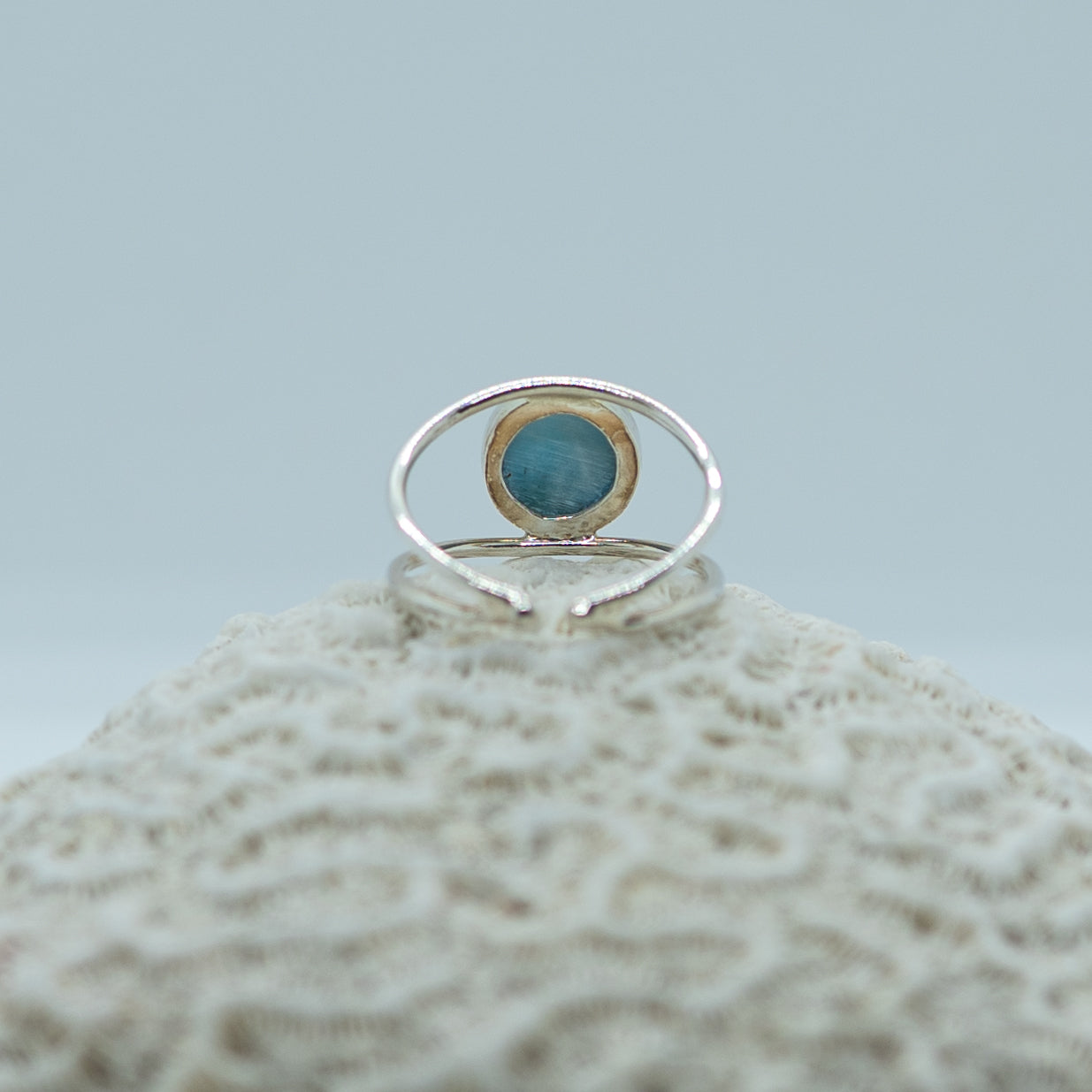 Photo d'une bague en argent 925 vu de dos et posée sur un coquillage. Bague non fermée qui se règle à la taille de votre doigt. Pierre de larimar ronde sertie sur le dessus.