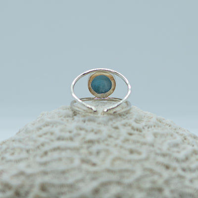 Photo d'une bague en argent 925 vu de dos et posée sur un coquillage. Bague non fermée qui se règle à la taille de votre doigt. Pierre de larimar ronde sertie sur le dessus.