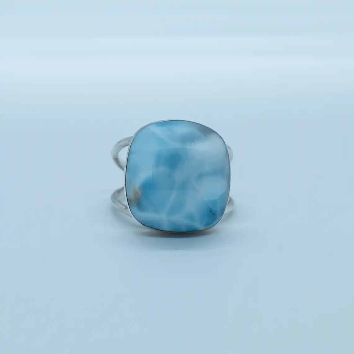 Bague en argent 925 avec une pierre de larimar de forme ronde, sur fond blanc. Bague réglable avec une structure de deux branches adaptable à toutes les tailles de doigts.