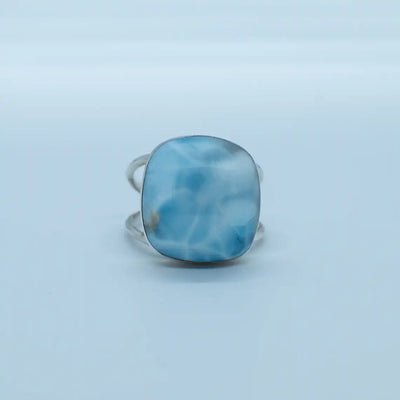 Bague en argent 925 avec une pierre de larimar de forme ronde, sur fond blanc. Bague réglable avec une structure de deux branches adaptable à toutes les tailles de doigts.