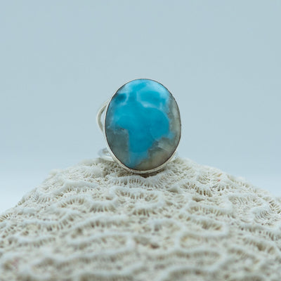 Bijou d'exception en argent 925 posé sur un coquillage et vue de face. Orné d'une pierre de larimar de République Dominicaine. Bague faite à la main par un artisan joaillier, plusieurs incrustations d'autres mineraux sont visible sur la pierre de larimar