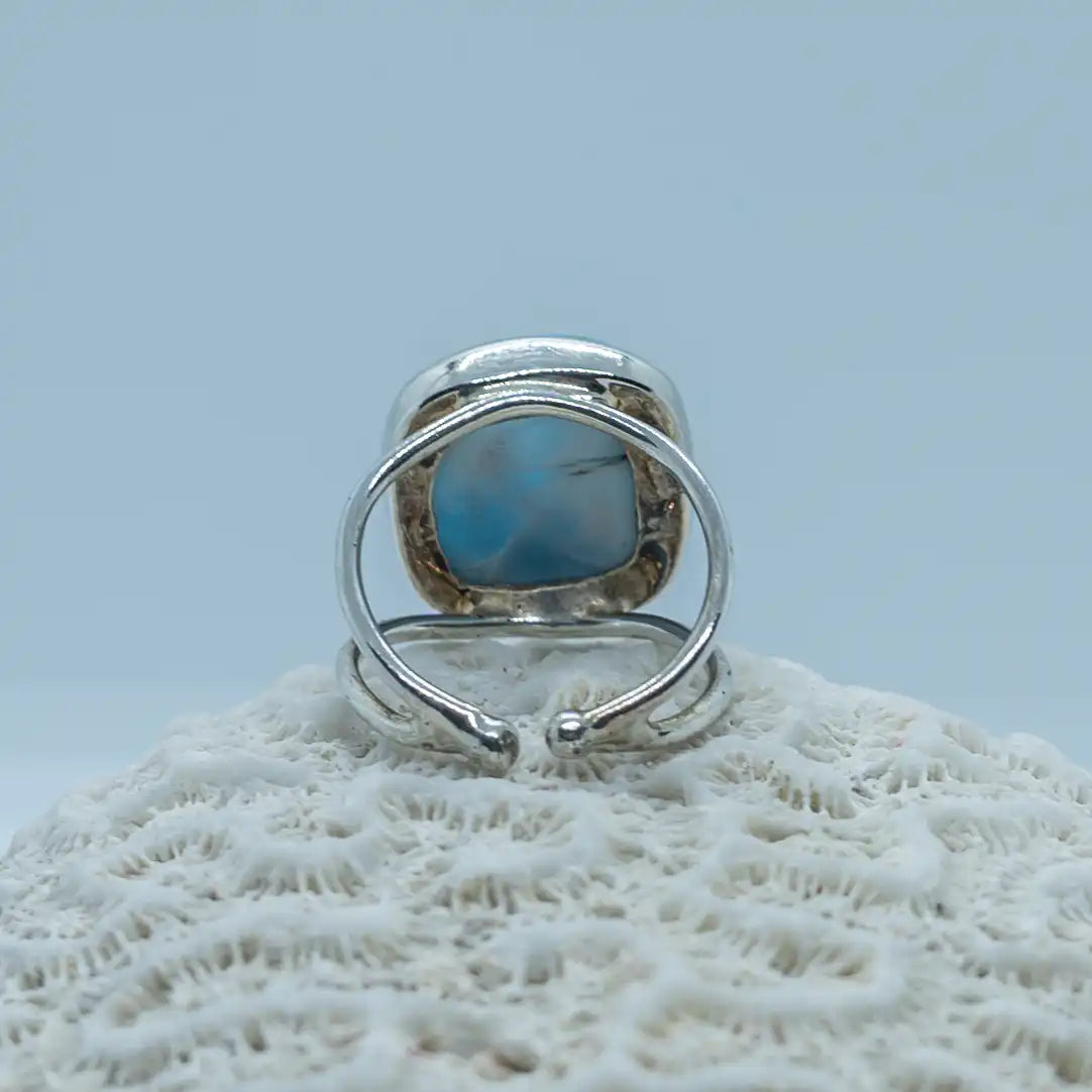 Bague d'exception en argent 925 vue de dos sur fond blanc. Bijou posé sur un coquillage vue de près, la bague est ouverte pour voir la pierre de larimar sous la bague et laisser passer l'énergie de cette pierre unique.