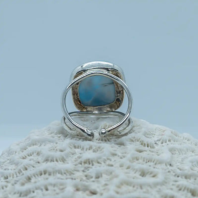 Bague d'exception en argent 925 vue de dos sur fond blanc. Bijou posé sur un coquillage vue de près, la bague est ouverte pour voir la pierre de larimar sous la bague et laisser passer l'énergie de cette pierre unique.