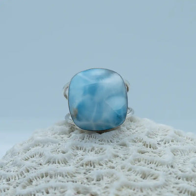 Bague posée sur un coquillage. Pierre de larimar de forme ronde montée sur cette bague en argent 925 réglable. Plusieurs nuances de bleu sur cette pierre de larimar de qualité supérieur.