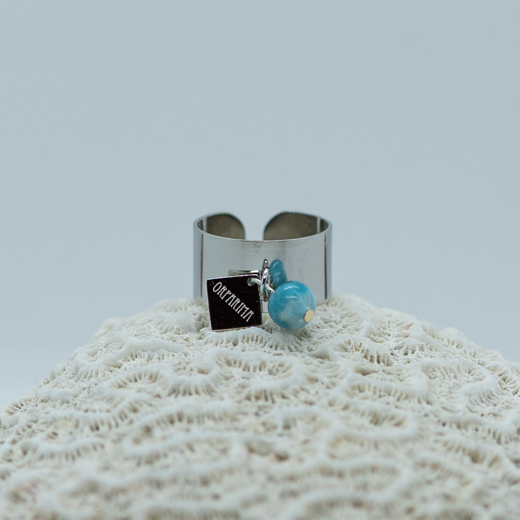 Bague posée sur un coquillage, de couleur argenté, faite en acier inoxydable 316L hypoallergénique. Bijou réglable ouvert sur le derrière, ne ternie pas. 