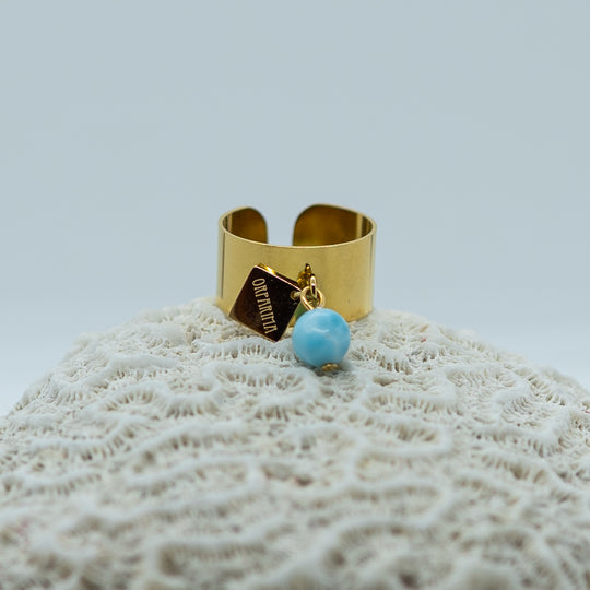 Bague dorée en acier inoxydable chirurgical 316L qui ne ternie pas. Perle de larimar bleu attachée à la bague avec une breloque Orparima. Bague ouvert pour être réglable. Bague lisse hypoallergéniques pour toutes les tailles de doigts.