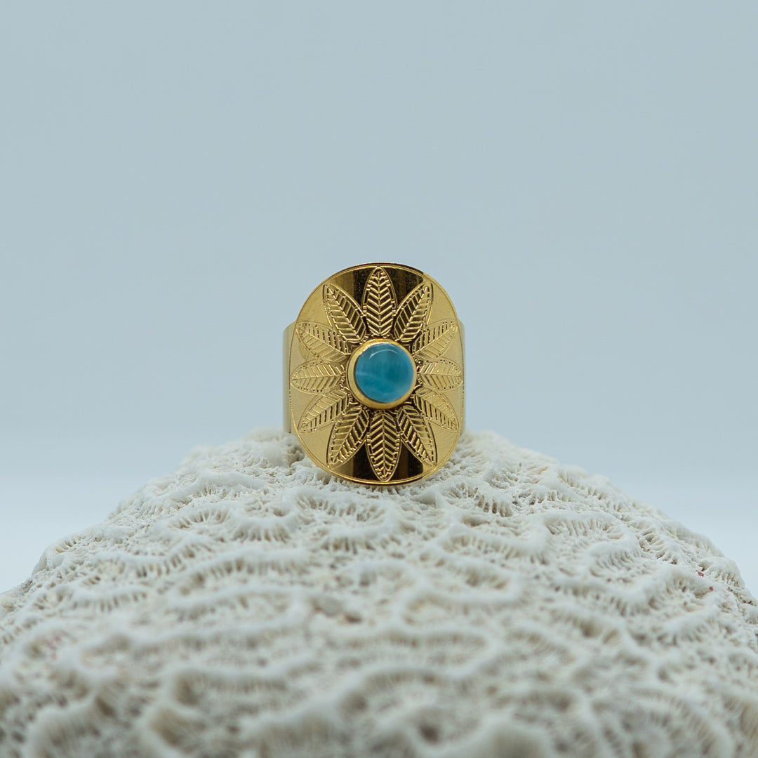 Bague de forme ovale avec une fleur gravé sur le dessus et une pierre de larimar ronde sertie en son centre. Bague en acier inoxydable 316L chirurgical qui ne ternie pas.