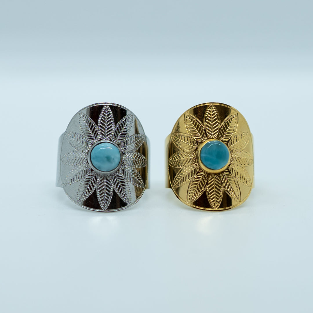 photo de deux bagues vue de face avec une pierre de larimar ronde au centre. Bagues en acier inoxydable 316L, l'une est dorée l'autre est argentée. Les deux bagues sont réglables. Motifs de fleur gravé sur chacune des bagues.