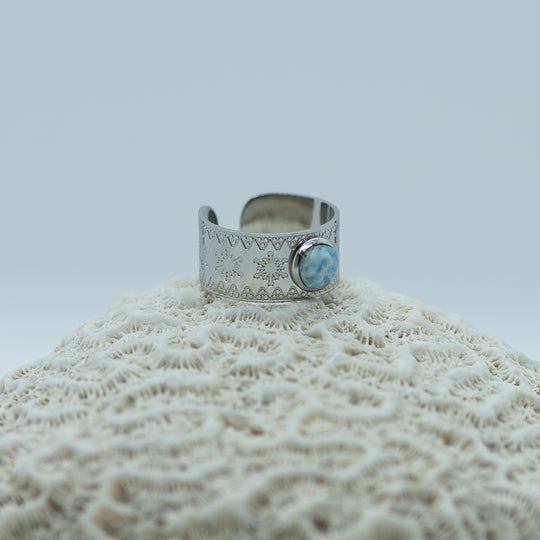 Bague posée de coté sur un coquillage. Bague en acier inoxydable chirurgical 316L couleur argent, ouverte pour se régler à plusieurs taille de doigts.