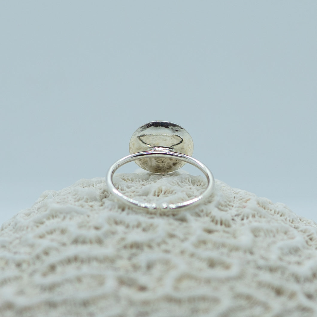 Bague posée sur un coquillage sur fond blanc. Bague en argent 925 ouverte sur le bas de l&