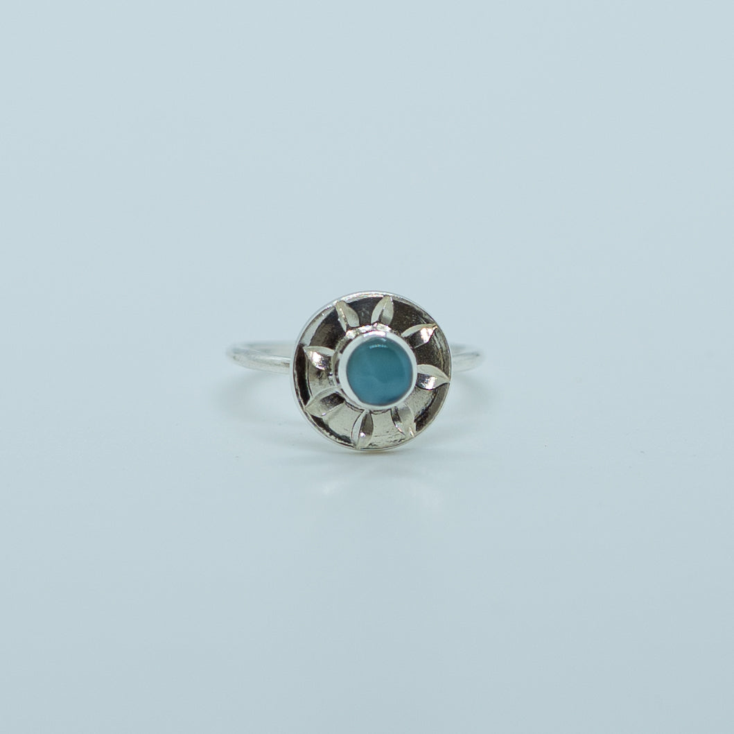Bague en forme de soleil sur fond blanc. Bague en argent 925 réglable et ajustable avec une pierre de larimar de forme ronde. Fait à la main en République Dominicaine.