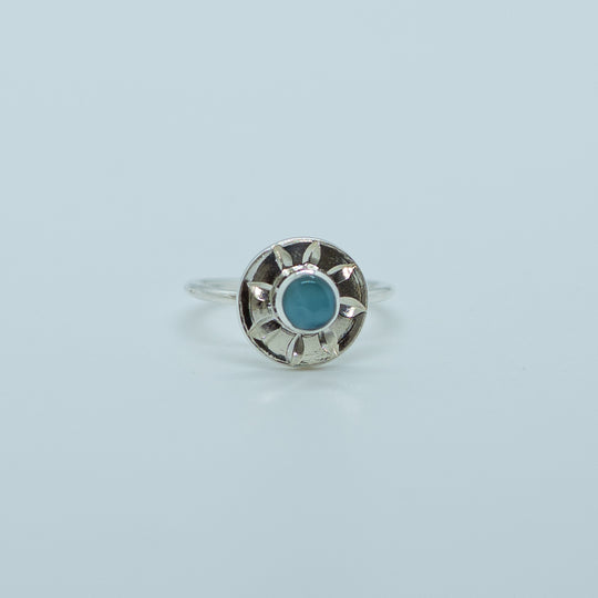Bague en forme de soleil sur fond blanc. Bague en argent 925 réglable et ajustable avec une pierre de larimar de forme ronde. Fait à la main en République Dominicaine.