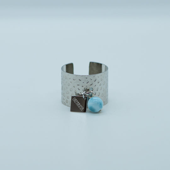 Bague avec une breloque orparima et une perle de larimar de 6mm de diamètre. Bague texturé argenté en acier inoxydable 316L réglable.