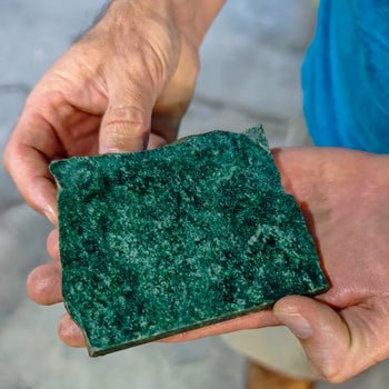 Morceau de pierre naturelle de Jade Jaguar Maya venant du Guatemala tenu dans les mains d'un homme. Pierre de couleur verte avec plusieurs nuances allant du vert clair au vert foncé presque noir.