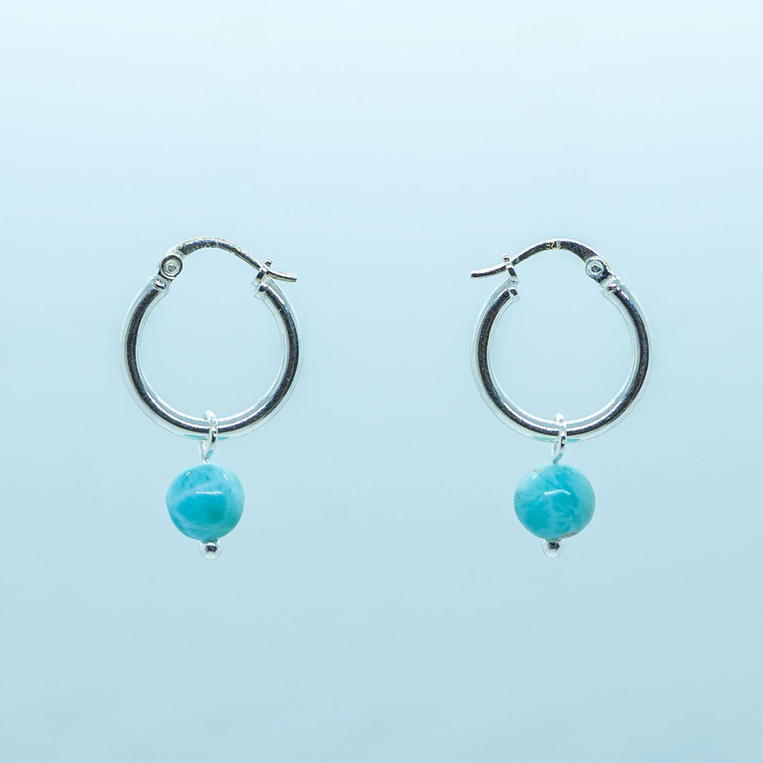 Photo d'une paire de boucles d'oreilles créoles avec une pierre de larimar bleue en pendant. Les créoles sont en argent 925. Larimar origine République Dominicaine.