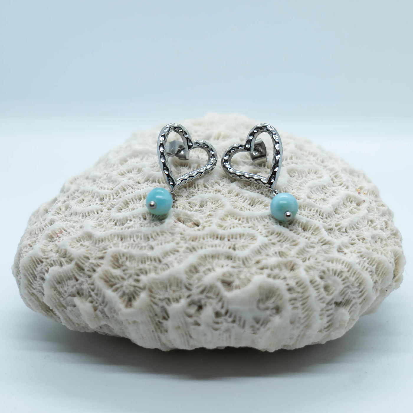 Paire de boucles d'oreilles en acier inoxydable 316L argenté et leur perle de Larimar bleu de République Dominicaine. Bijou en forme de cœur texturé avec son Larimar.