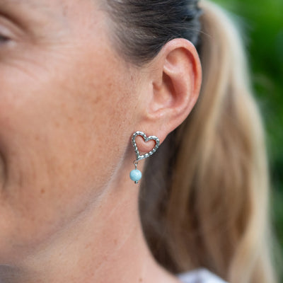 Femme portant du Larimar sur une boucle d'oreille en forme de cœur texturé, fait en acier inoxydable 316L argenté. Bijou fait main en République Dominicaine.