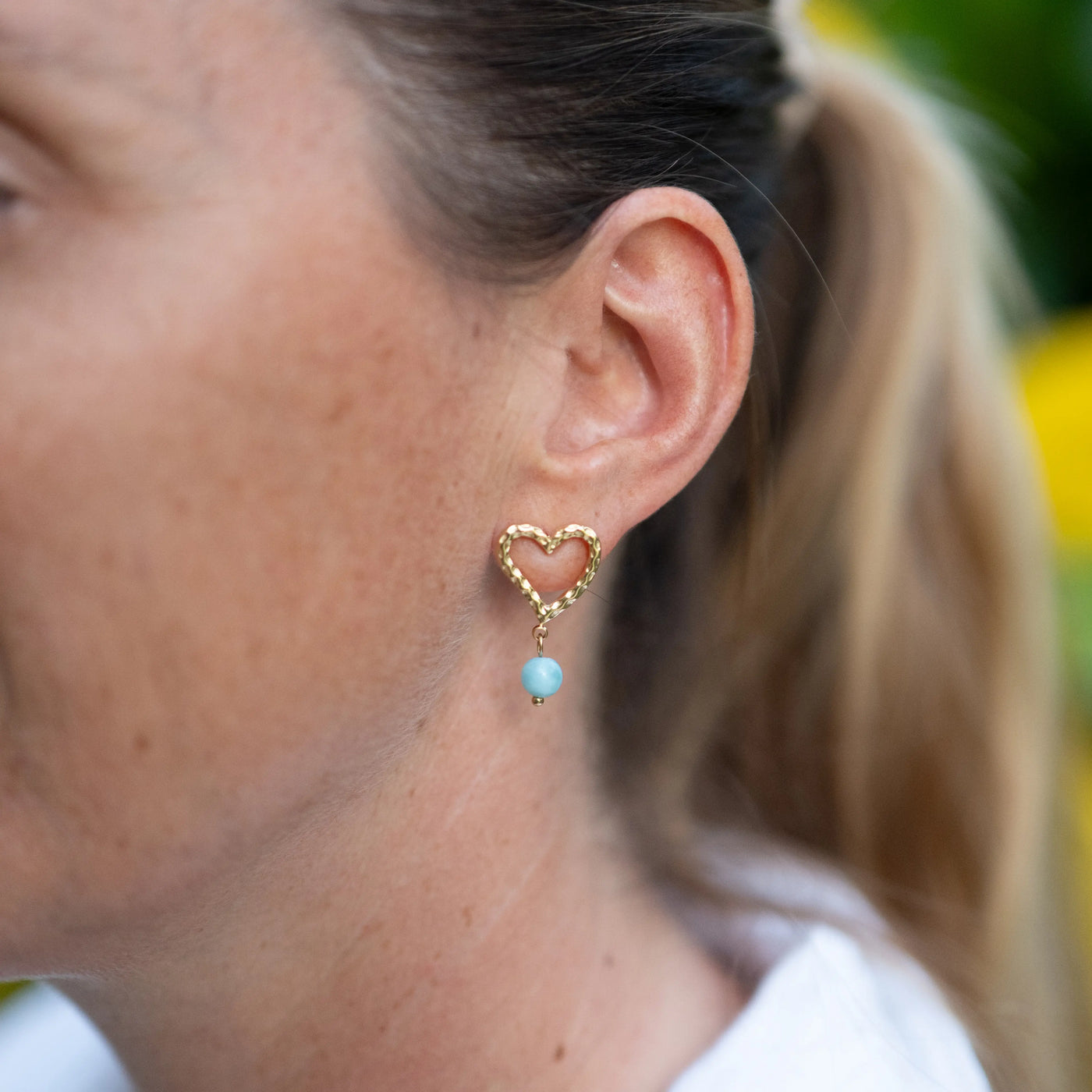 Femme portant une boucle d'oreille en forme de cœur texturé comprenant une perle de Larimar en pendant. Boucle portée par une femme, bijou artisanal avec du Larimar.