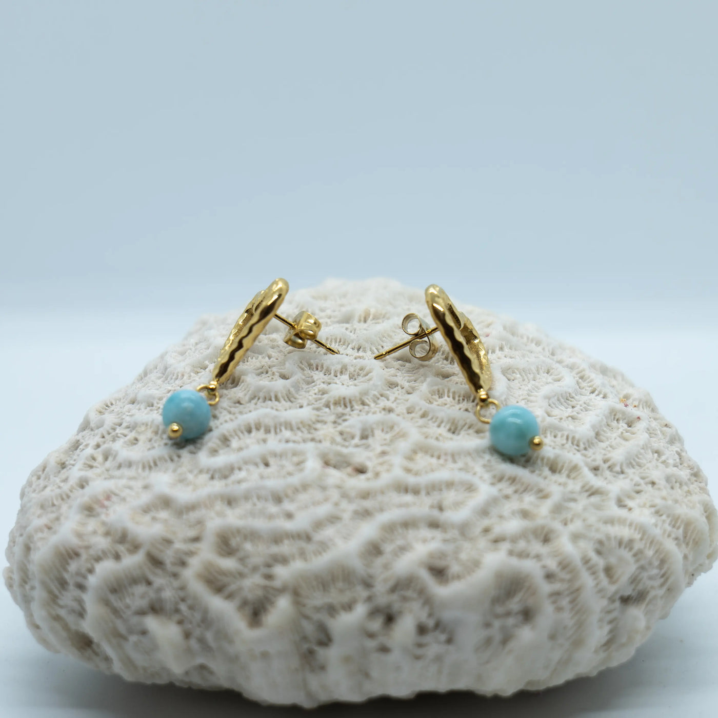 Vue de profil d'une paire de boucles d'oreilles en acier inoxydable 316L avec leur perle de Larimar de République Dominicaine. Boucles d'oreilles dorées et Larimar bleu.
