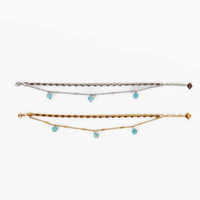 Photo de deux bracelets en acier inoxydable 316L, l'un est argenté l'autre est doré. Ces deux bracelets sont composés de deux chaines et comportent trois perles de larimar pendantes. Extension de chaine avec breloque orparima.