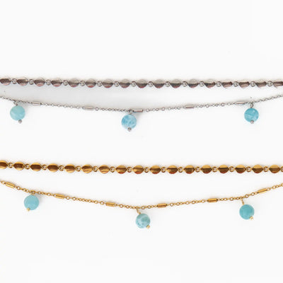 Photo de deux bracelets ouverts posés à plat sur fond blanc. Bracelets composés de deux chaîne différentes avec trois perles de larimar pendantes. Extension de chaîne avec une breloque orparima. Les chaînes sont en acier inoxydable 316L.
