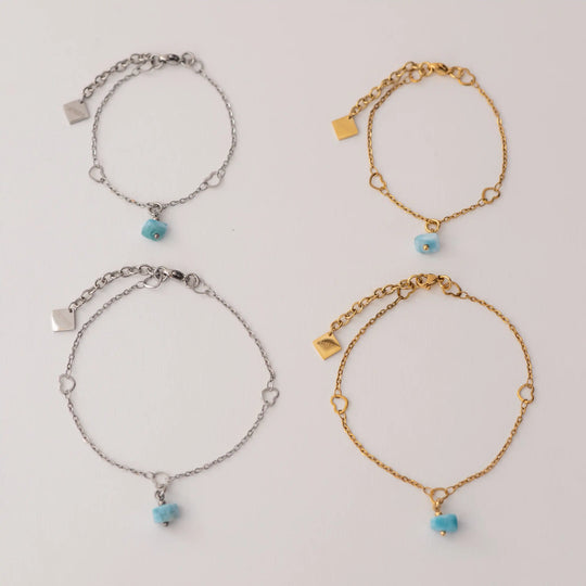 Photo de quatre bracelets, deux argentés et deux dorés, vues de haut. Chaque bracelet possède un fragment de pierre de larimar en pendant ainsi qu&