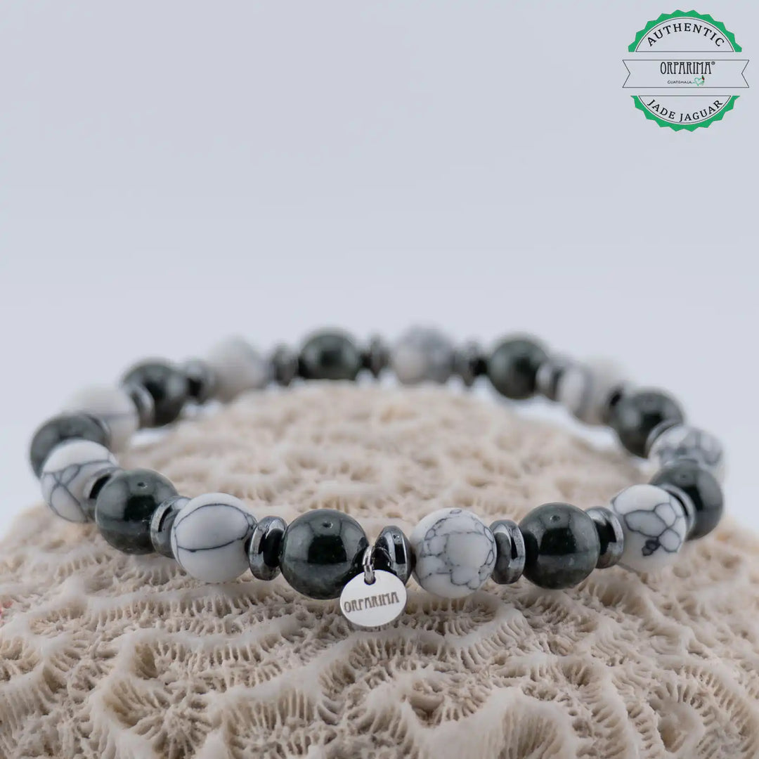 Bracelet avec une alternance de Jade Jaguar du Guatemala et de Howlite blanche posé sur un coquillage de couleur blanche. Bracelet en fil élastique très résistant avec sa breloque Orparima pour certifier son origine.