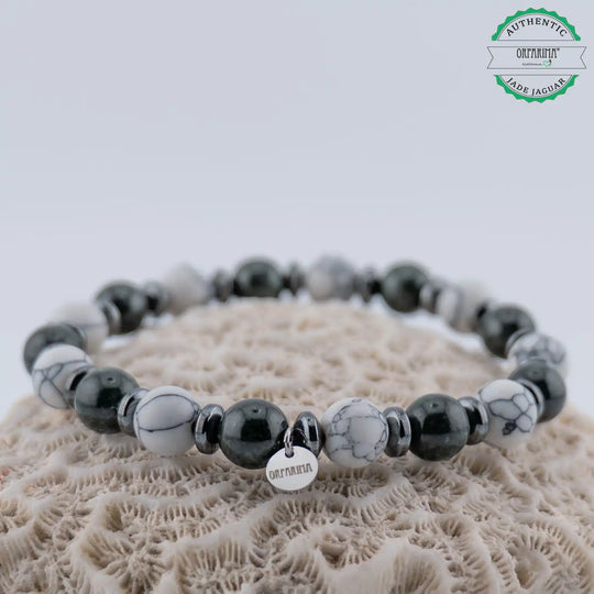 Bracelet avec une alternance de Jade Jaguar du Guatemala et de Howlite blanche posé sur un coquillage de couleur blanche. Bracelet en fil élastique très résistant avec sa breloque Orparima pour certifier son origine.