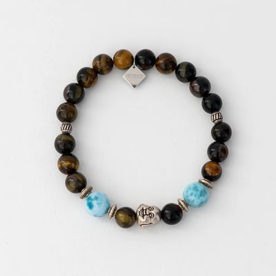 Bracelet en oeil du tigre monté sur un fil élastique avec deux perles de larimar et une breloque en forme de tête de bouddha. Breloque orparima pendante.