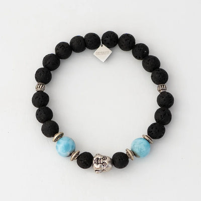 Photo d'un bracelet posé à plat sur un fond blanc. Bracelet en pierre de lave avec une breloque tête de bouddha et deux perles de larimar de 11mm de diamètre.