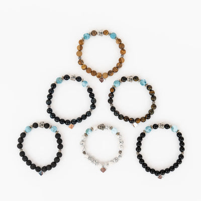 Photo de six bracelets élastique fait chacun avec des pierres différentes parmi la howlite, pierre de lave, obsidienne, œil du tigre, Jaspe paysage ou œil du faucon. Bracelet avec une breloque bouddha et deux perles de larimar de 9mm de diamètre environ.