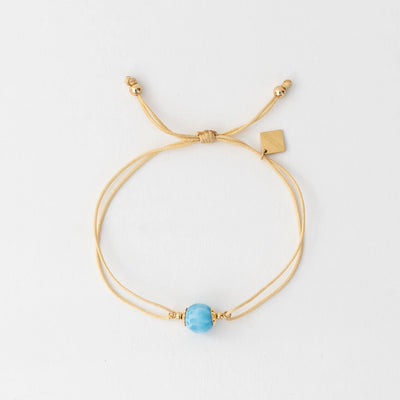 Photo d'un bracelet en cordon doré avec une perle de larimar bleu et une breloque orparima. Bracelet réglable adaptable à plusieurs tailles de poignets. Résiste à l'eau et à la transpiration.