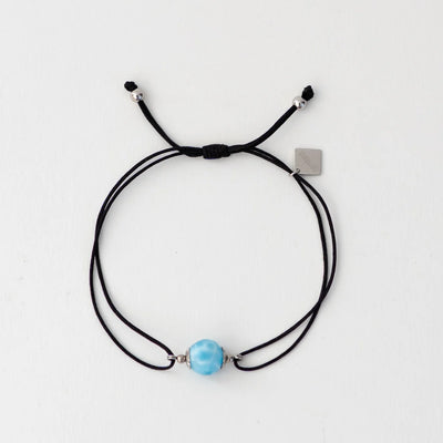 Bracelet en cordon noir avec une perle de larimar bleu faite à la main par notre artisan dominicain. Breloque orparima pendante. Resiste à l'eau et à la transpiration.