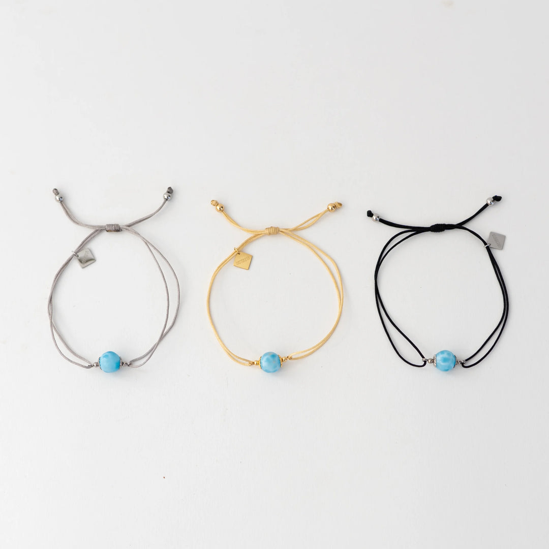 Bracelets cordon disponibles en trois couleurs différentes, argenté, doré ou noir. Bracelet avec chacun une perle de larimar et une breloque orparima en pendant.