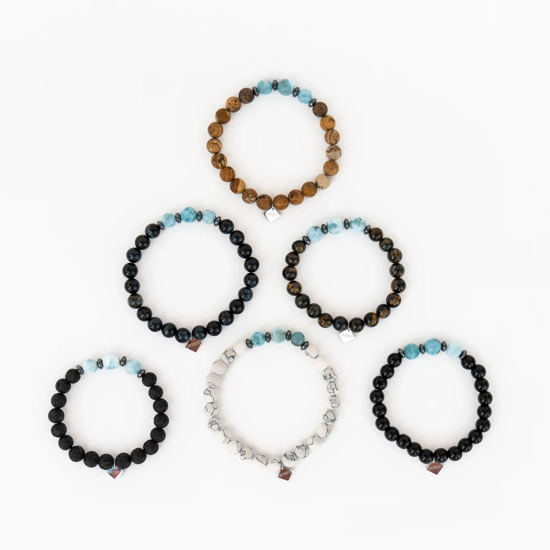 Photo de six bracelets avec trois perles de larimar chacun. Chaque bracelet possède une pierre spécifique, howlite, pierre de lave, obsidienne, oeil du tigre, oeil du faucon ou Jaspe paysage.