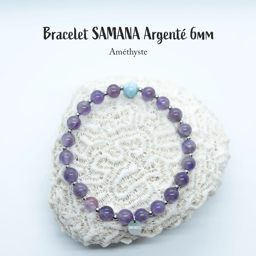 Bracelet en perles de 6mm en améthyste avec une perle de Larimar de République Dominicaine, de couleur bleue, posé sur un coquillage de couleur blanc, sur fond blanc. Chaque perle est séparée de la suivante par une petite perle en acier inoxydable argenté.