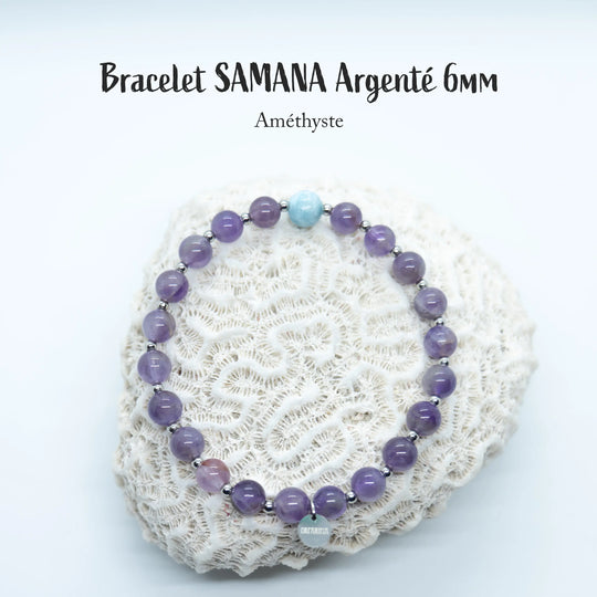 Bracelet en perles de 6mm en améthyste avec une perle de Larimar de République Dominicaine, de couleur bleue, posé sur un coquillage de couleur blanc, sur fond blanc. Chaque perle est séparée de la suivante par une petite perle en acier inoxydable argenté.