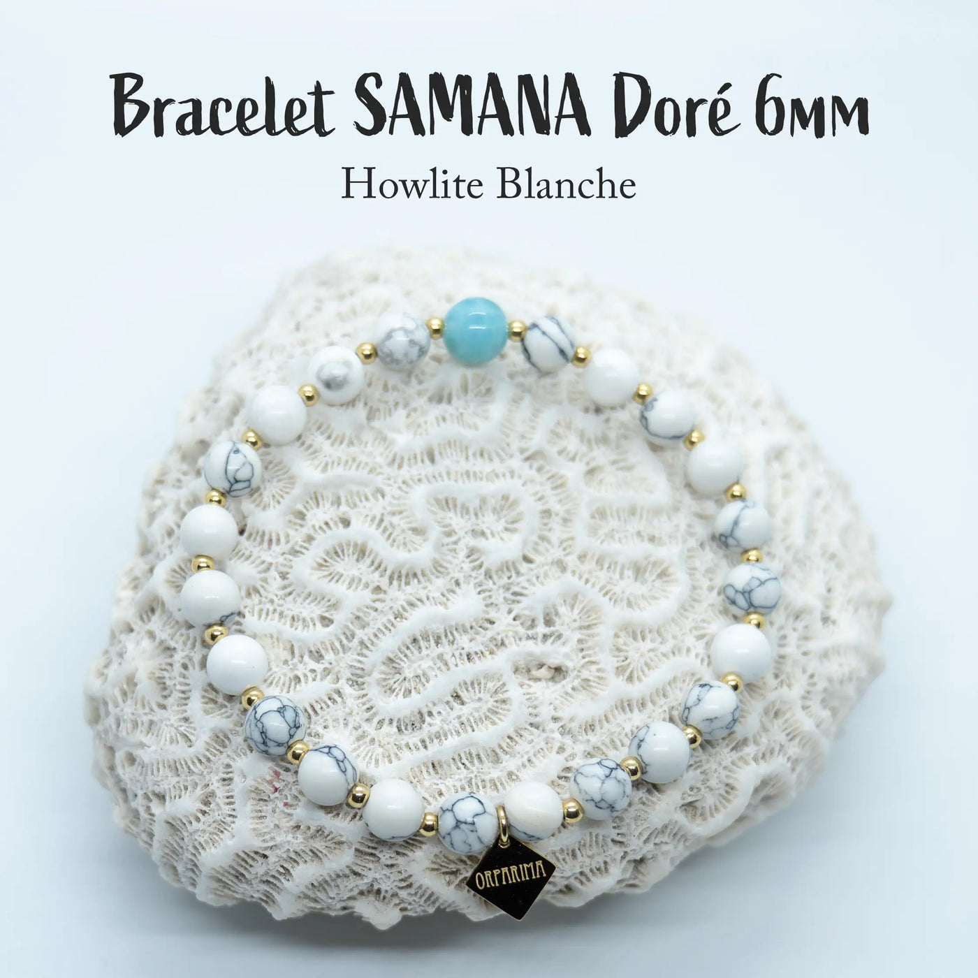 Bracelet en fil élastique fait à la main en République Dominicaine. Ce bracelet est composé de perles de howlite blanche et d'une perle de Larimar. Toutes les perles sont séparées entre elles par une petite perle en acier inoxydable doré. Bijou posé sur un coquillage blanc sur fond blanc.
