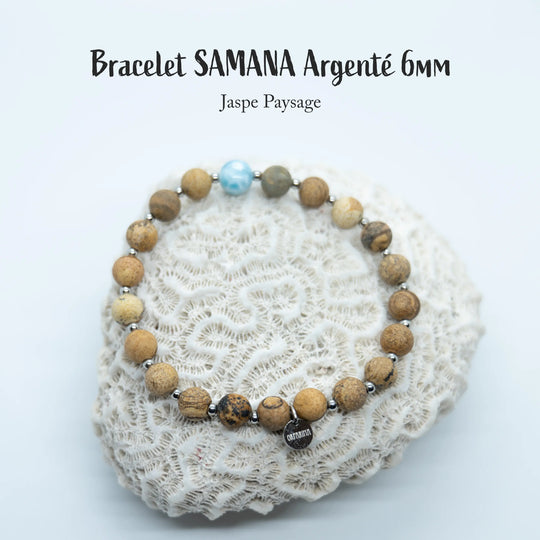 Coquillage blanc sur lequel est posé un bracelet avec des perles de 6mm de jaspe paysage et une perle de Larimar de couleur bleu. Bijou fait à la main avec un fil élastique disponible en plusieurs tailles.