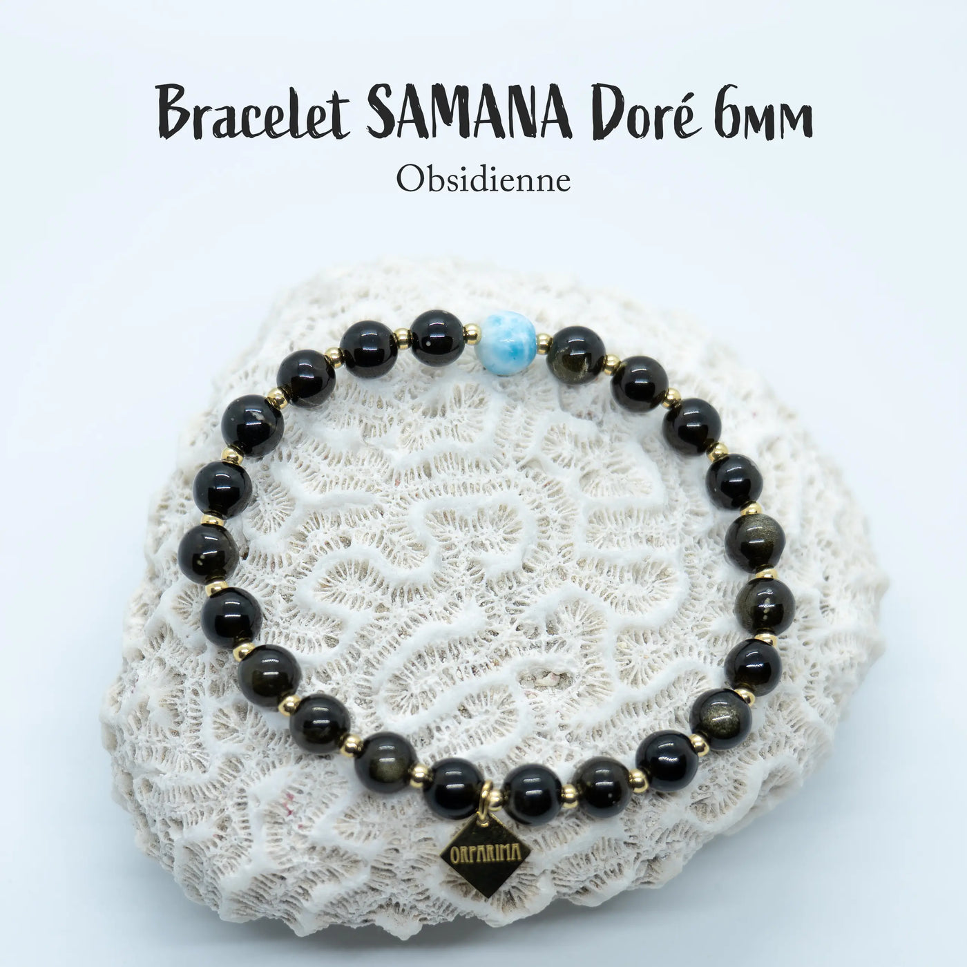 Bracelet fait à la main, composé de perle d'obsidienne et d'une perle de Larimar. Les perles de ce bracelet sont d'un diamètre de 6mm. Ce bijou est posé sur un coquillage et possède une breloque gravé orparima.