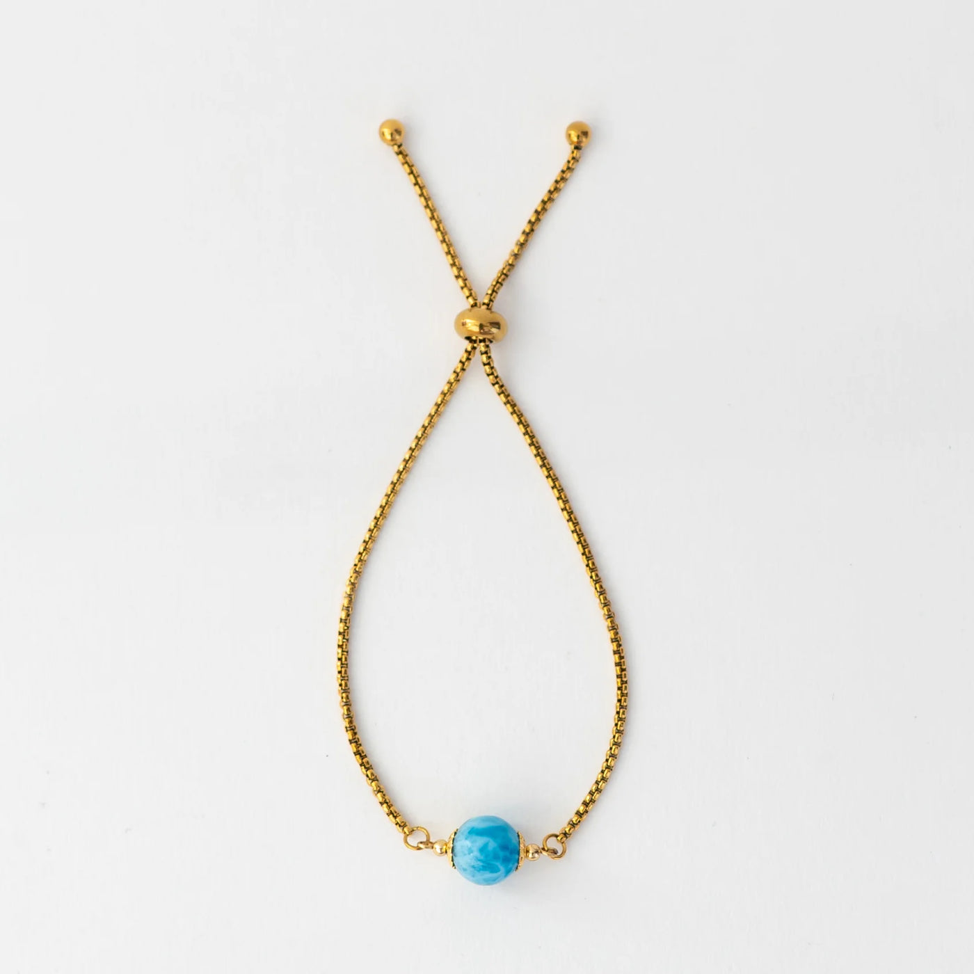 Photo d'un bracelet doré en acier inoxydable 316L et de sa perle de larimar bleue. Bracelet réglable avec un système de fermeture coulissant.