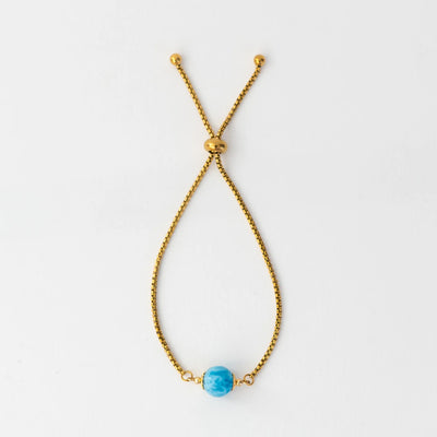 Photo d'un bracelet doré en acier inoxydable 316L et de sa perle de larimar bleue. Bracelet réglable avec un système de fermeture coulissant.