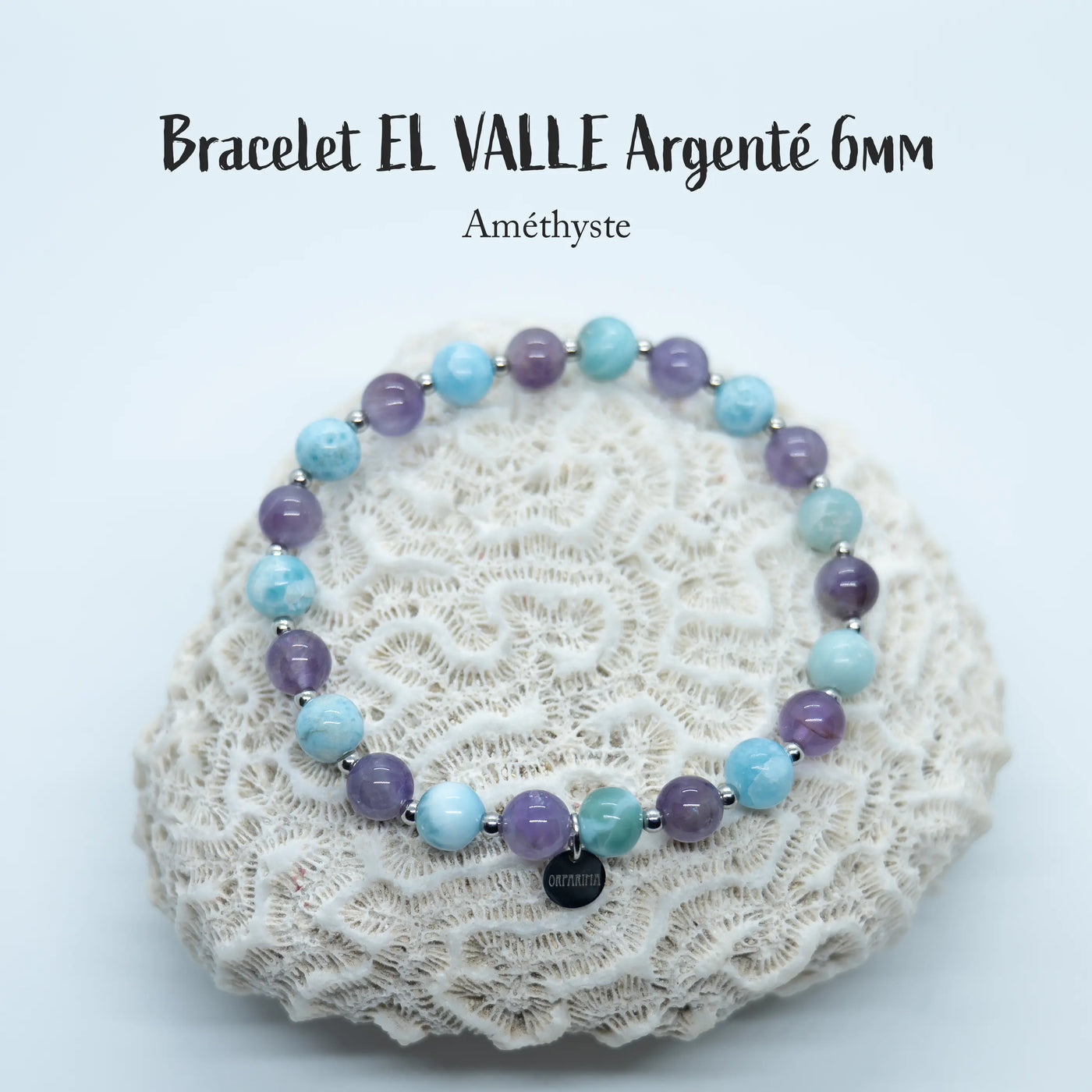 Bracelet posé sur un coquillage, fait à moitié en améthyste et l'autre moitié en perles de Larimar. Ce bracelet est en fil élastique et peut être fait en plusieurs tailles, il possède une breloque en acier inoxydable avec orparima gravé dessus. Les perles sont en 6mm.