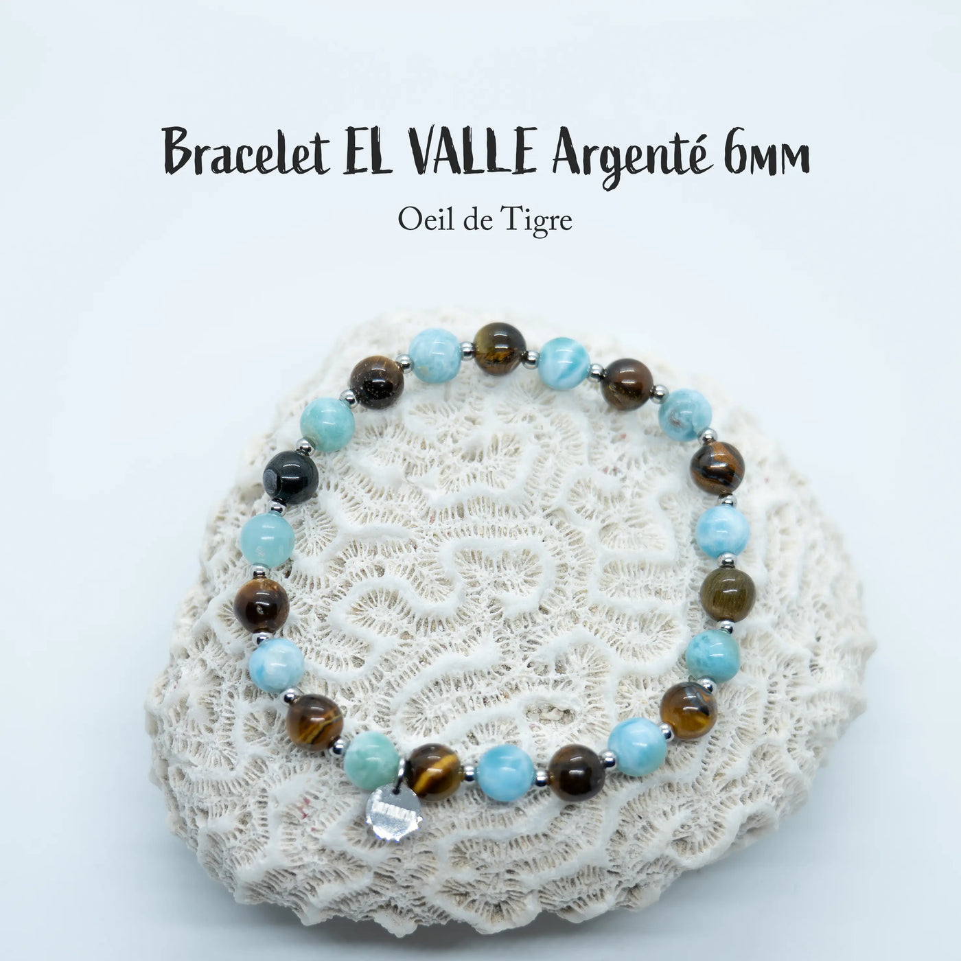 Bracelet avec une alternance de perles de Larimar et d’œil du tigre séparées par des petites perles en acier inoxydable argenté. Bijou posé sur un coquillage de type corail, fait avec un fil élastique.