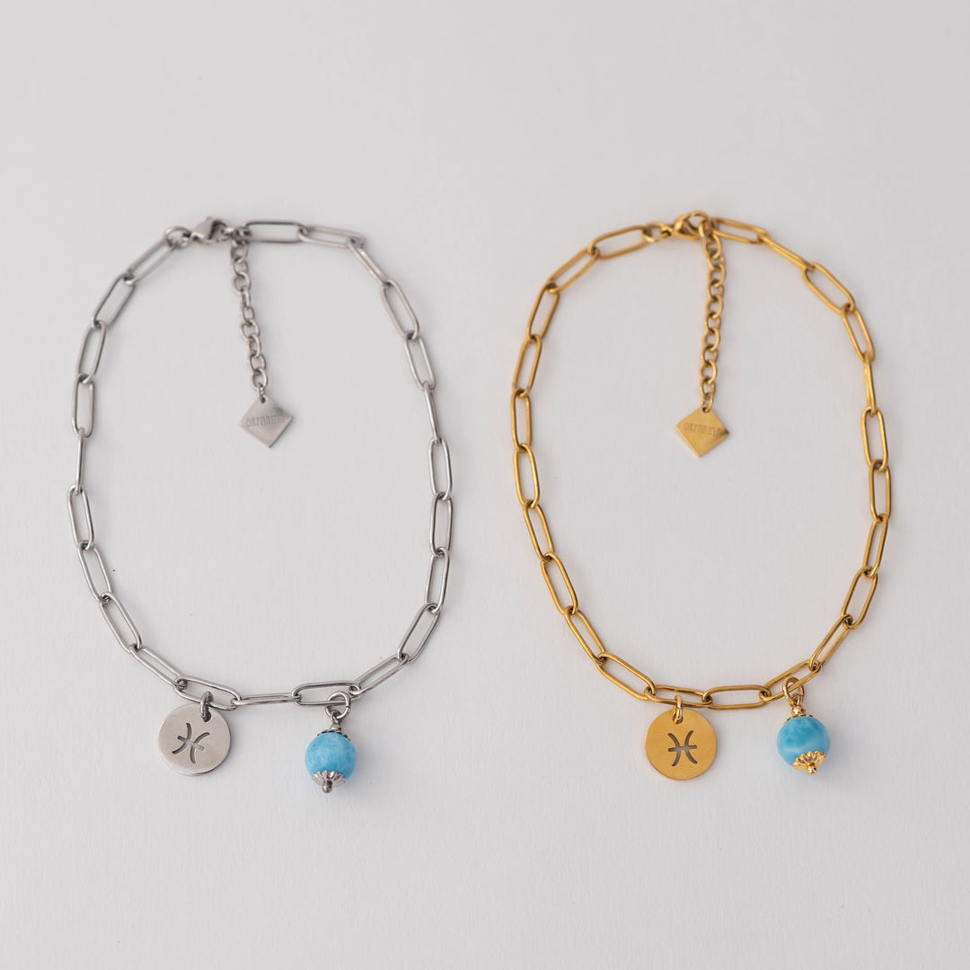 Photo de deux bracelet de cheville fermés, posés sur un fond blanc. Bracelets en acier inoxydable 316L argenté ou doré. Extention de chaine avec une breloque orparima sur le bout. Deux breloques sont attachées à la chaine via un anneau, une perle de larimar de 6mm et un signe astrologique.