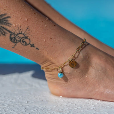 Bracelet de cheville porté sur la cheville droite d'une femme, orné d'un signe astrologique et d'une perle de larimar en breloque. Bijou résistant à la corrosion avec un signe astrologique personnalisable.